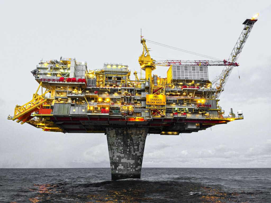 A well-lit offshore oil platform against a cloudy sky in Norway's waters.